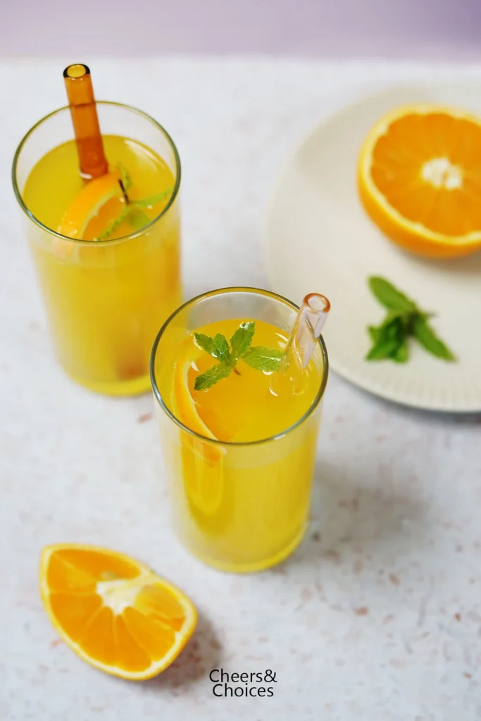 Selbstgemachte Orangen-Limonade auf zwei Gläser verteilt, mit Minze und Orangen-Scheiben als Garnitur.