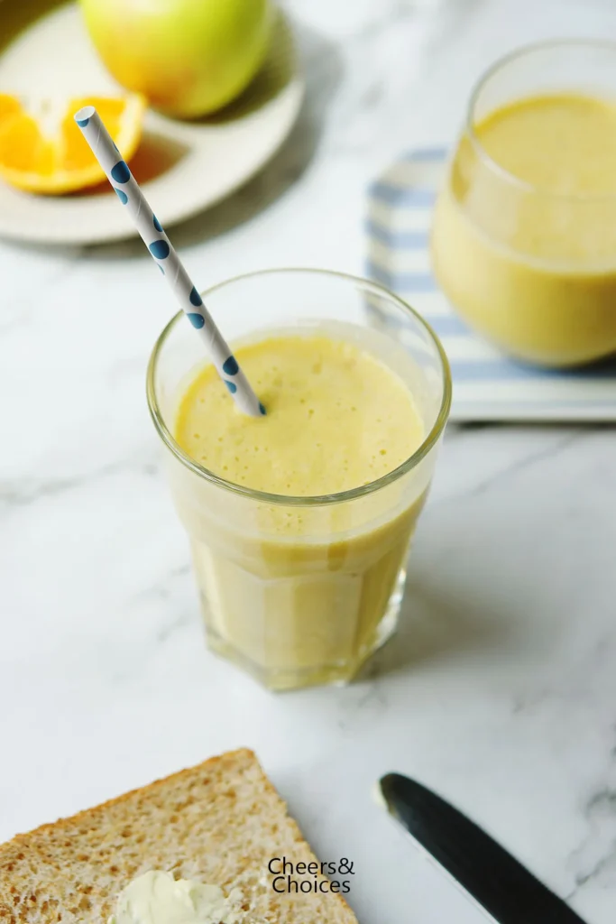Smoothie mit Apfel und Banane in einem hohen Glas, auf dem Frühstückstisch.